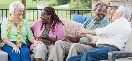 group of female and male seniors sitting on an outdoor sofa on a patio chatting