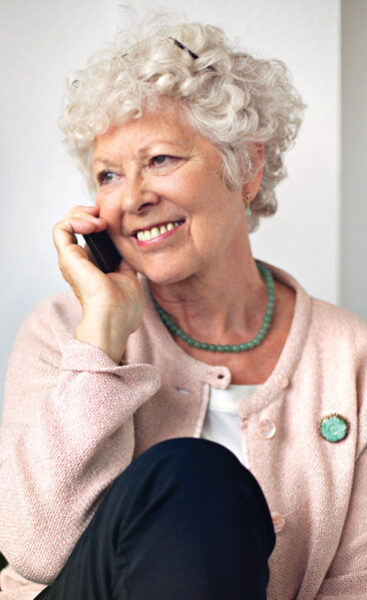 Older adult woman sitting, with a telephone up to her ear, smiling during conversation